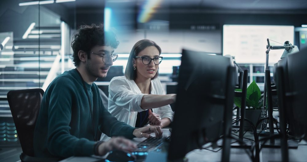 A man and a woman are discussing something on a computer screen.