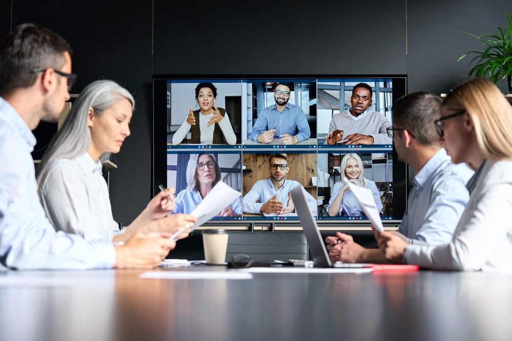 People in an office are having a meeting with six people joining remotely on a TV screen.